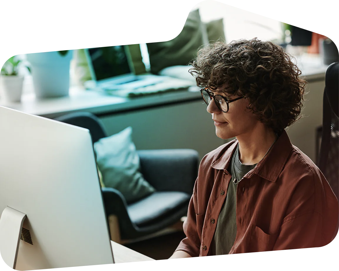 Young Professional Woman Working on Her Computer in a Cozy Office Space Woman with curly hair and glasses working on a computer in a modern office environment.